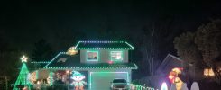 A house fully decorated with green and white Christmas lights, featuring a large tree, candy cane pathway, and festive inflatables